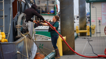 image describes someone fueling or working on a vehicle at one of Petro Marine's fueling stations around Alaska. She is a technician and possibly a machine operator.